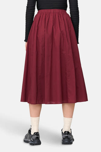 Bordeaux rok van 24 colours gmbh met elastische tailleband, gedragen met een zwarte top, crèmekleurige sokken en zwarte sneakers.
