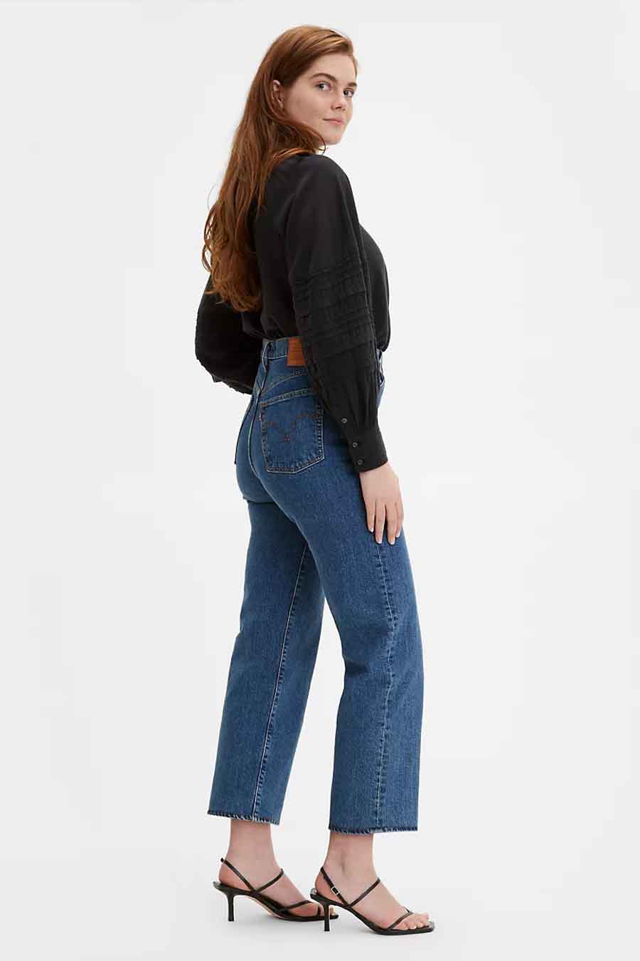 Rechte jeans in middenblauw denim van Levi's met hoge taille, gecombineerd met een zwarte blouse en sandalen met hak.
