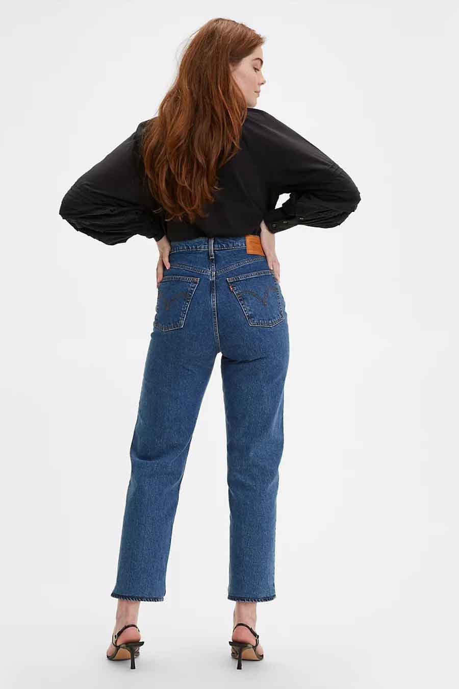 Rechte jeans van midblauw denim van Levi's, met achterzakken en bruin leren patch, gedragen met een zwarte blouse en hakken.
