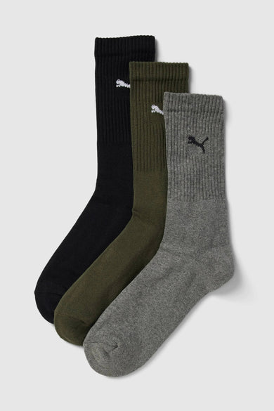 Chaussettes vertes PUMA à structure côtelée avec petit logo, à côté de variantes noires et grises, posées à plat sur fond clair