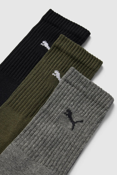 Chaussette côtelée verte de PUMA avec logo blanc, à côté de variantes noires et grises, posée à plat sur fond clair