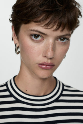 Blauwe trui met ronde hals van MANGO, met een gestreept patroon en gedragen met zilveren oorringen.
