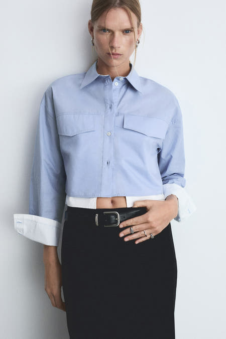 Blauw hemd met lange mouwen van MANGO, cropped en gedragen met een zwarte rok en zilveren ringen.
