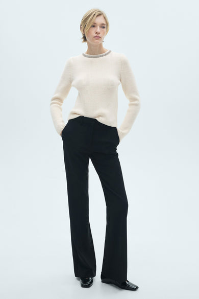 Pull-over blanc à col rond de MANGO, avec structure en côtes et détail strass autour du col, porté avec un pantalon noir et des chaussures.