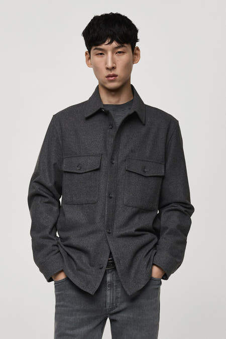 Chemise grise à manches longues de MANGO, avec deux poches po po et portée avec un jean gris.