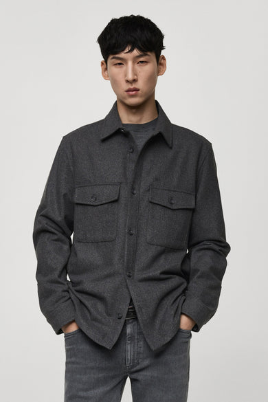 Chemise grise à manches longues de MANGO, avec deux poches po po et portée avec un jean gris.