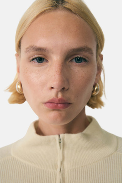 Witte coltrui van MANGO, close-up van een model met gouden oorbellen.
