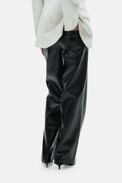 Zwarte broek met crocoprint van MANGO, gecombineerd met een witte blazer, achteraanzicht.
