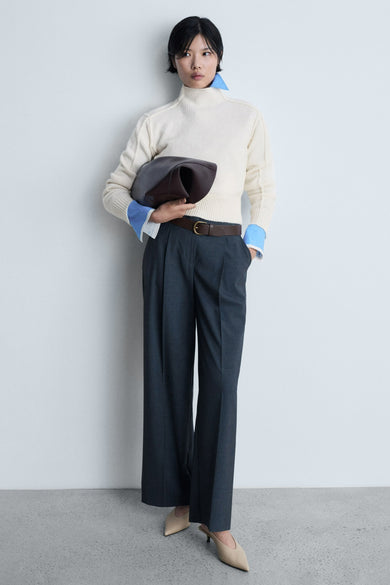Witte trui met ronde hals van MANGO, gedragen met een blauw overhemd en donkergrijze pantalon met plooien.