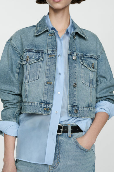 Jeansjas van midblauw denim van MANGO, met lange mouwen en klepzakken, gecombineerd met een blauw overhemd en een zwarte riem.
