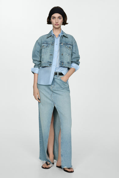 Denim jeansjas van MANGO, met een lichtblauwe wassing, gedragen over een lichtblauw overhemd en een lange denim rok met split.
