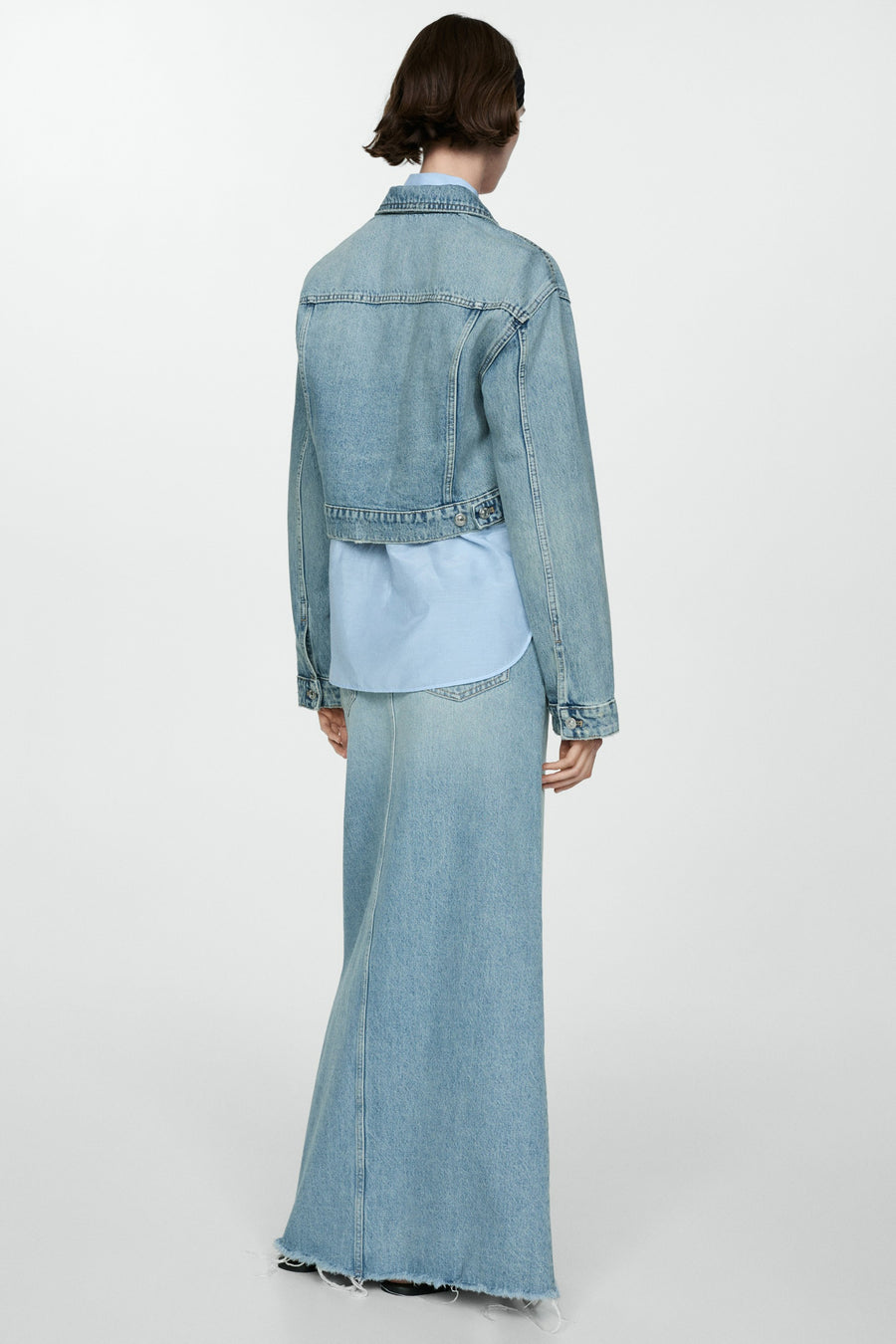 Jeansjas van mid blue denim van MANGO, rugaanzicht, gecombineerd met een lichtblauwe blouse en een bijpassende lange rok met gerafelde zoom.
