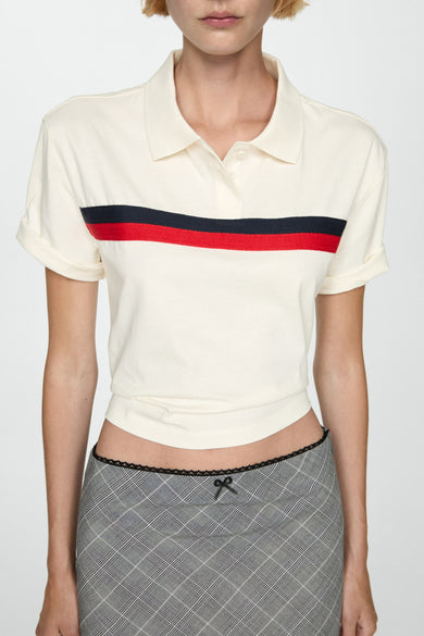 Witte polo met korte mouwen van MANGO, met een rode en zwarte streep, gedragen met geruite minirok.
