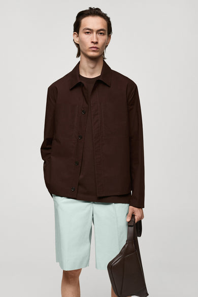 Rode korte jas van MANGO, gedragen over een bruin T-shirt en lichtgroene shorts, met een bruine schoudertas.
