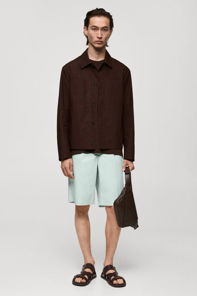 Korte rode jas van MANGO, met lange mouwen, gedragen over een T-shirt en lichte shorts met een leren tas en sandalen.
