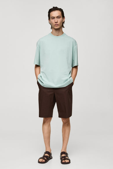 Blauw T-shirt met korte mouwen van MANGO, gecombineerd met bruine shorts en leren sandalen.

