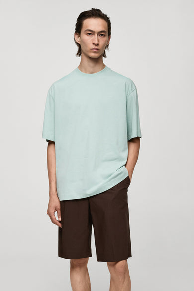 Blauw T-shirt met korte mouwen van MANGO, gedragen met bruine shorts, staand tegen een egale achtergrond.
