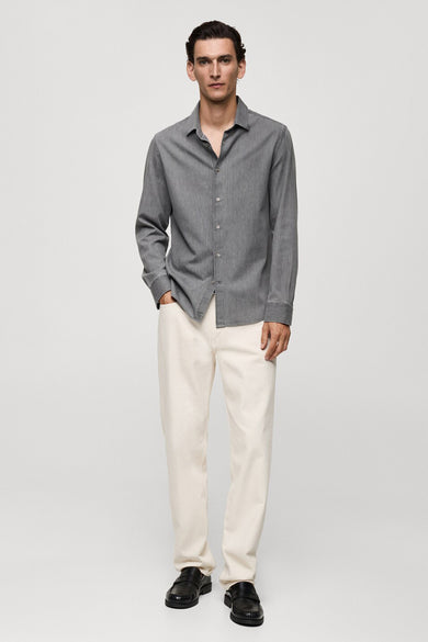 Grijs jeanshemd van MANGO, met lange mouwen en gedragen met een witte jeans en zwarte loafers.
