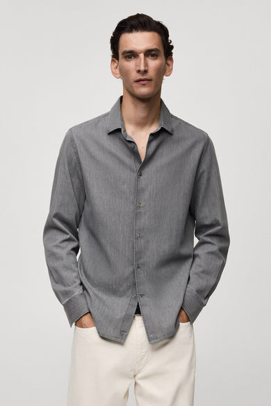 Grijs jeanshemd van MANGO, met lange mouwen, knoopsluiting en gedragen met een witte jeans.
