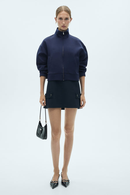 Blauw gilet van MANGO, gedragen met een bijpassende rok met zakken en zwarte pumps met riem.
