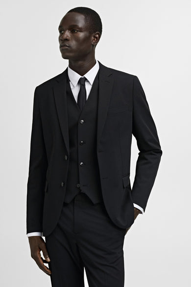 Zwarte blazer van MANGO, met een enkele rij knopen, gedragen over een vest, hemd en stropdas.