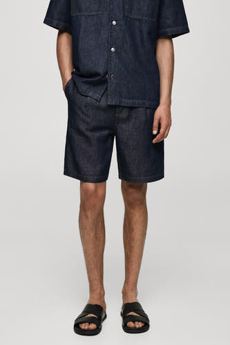 Denim jeansshort van MANGO, in mid blue, gedragen met een denim shirt en zwarte sandalen.