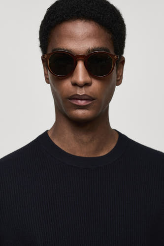 T-shirt bleu avec col rond de MANGO, porté avec un pull rayé foncé et des lunettes de soleil marron.