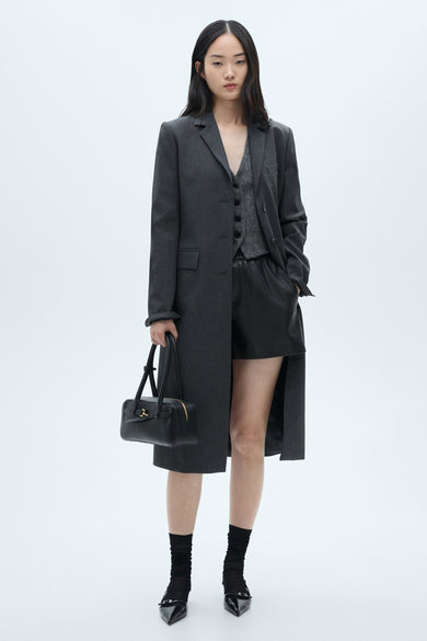 Multikleurige bermuda van MANGO, gecombineerd met een grijze vest, blazer en lange jas, zwarte sokken en schoenen, met zwarte tas.
