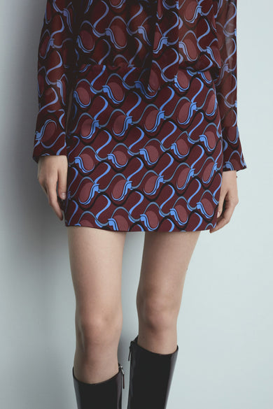 Korte rode rok van MANGO met golvend blauw patroon en gedragen met zwarte laarzen.
