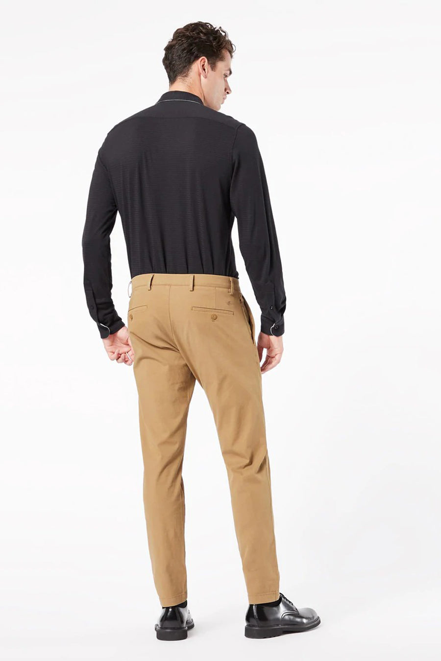 Man van achteren in bruine broek, zwarte longsleeve en zwarte schoenen.