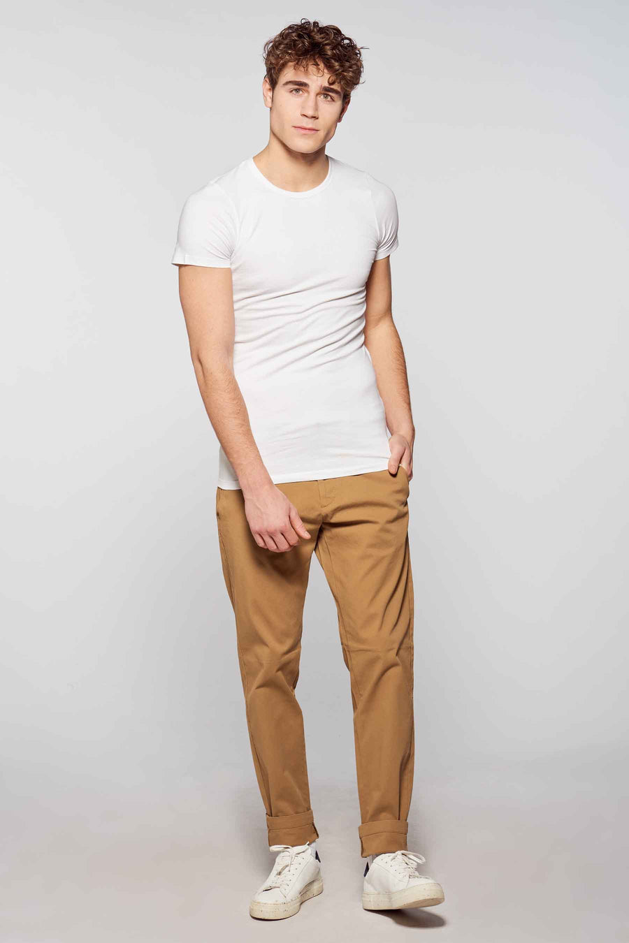 Man in witte T-shirt en bruine broek.