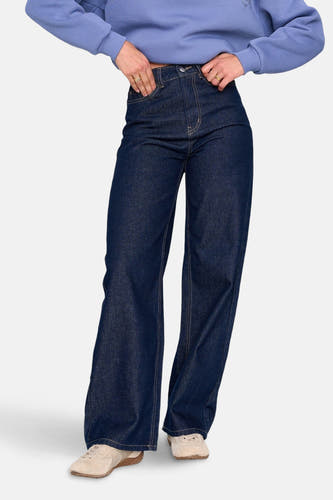 Donkerblauwe denim jeans met wijde pijpen van 24 colours gmbh, met beige schoenen en een blauwe trui.
