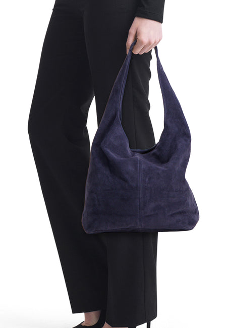Sac à bandoulière bleu marine effet daim d'Access®, tenu par une personne vêtue de noir, avec surpiqûres verticales.