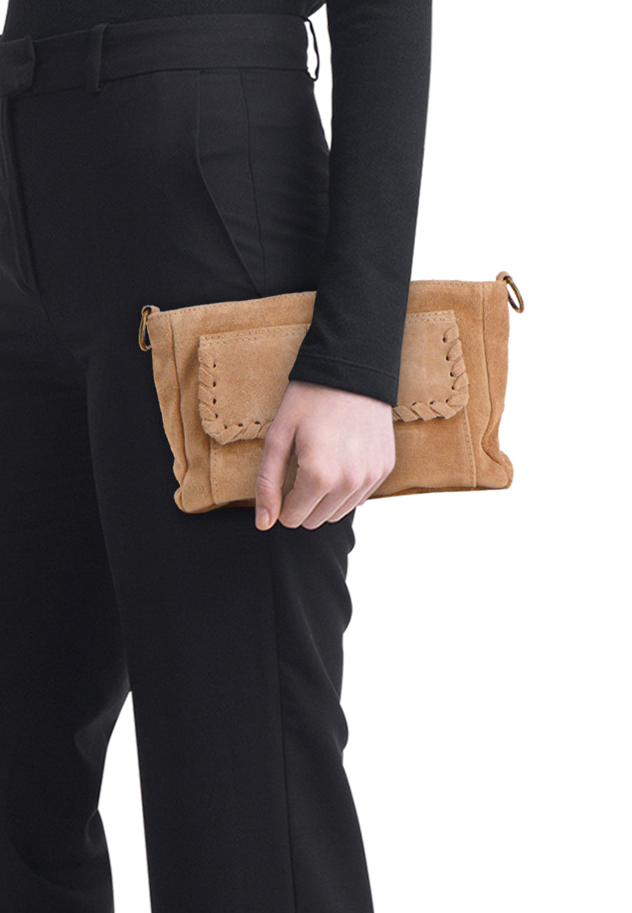 Beige suède schoudertas van Access® met gevlochten stiksels op de klep, vastgehouden tegen een zwarte broek.