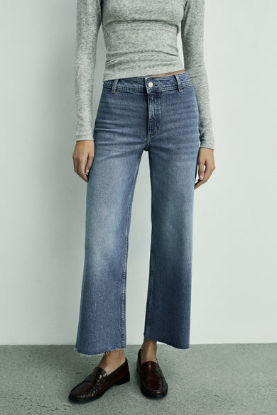 Donkerblauwe wijde jeans van MANGO, met afgewerkte randen en een lange grijze top.
