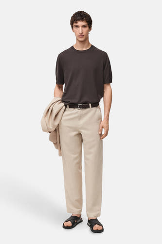 Jean écru de MANGO, avec une ceinture noire, associé à des sandales noires et un T-shirt marron.