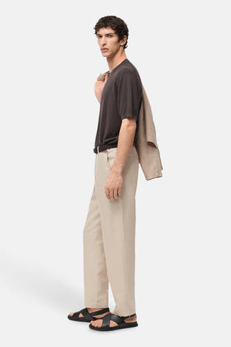 Jean écru de MANGO, porté avec un t-shirt marron et des sandales noires, avec une veste beige sur l'épaule.