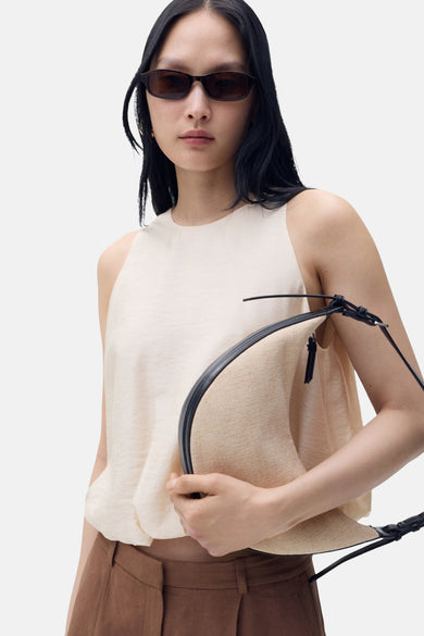 Blouse sans manches beige de MANGO, drapée à l'avant et associée à un pantalon marron et une lunette de soleil ovale.