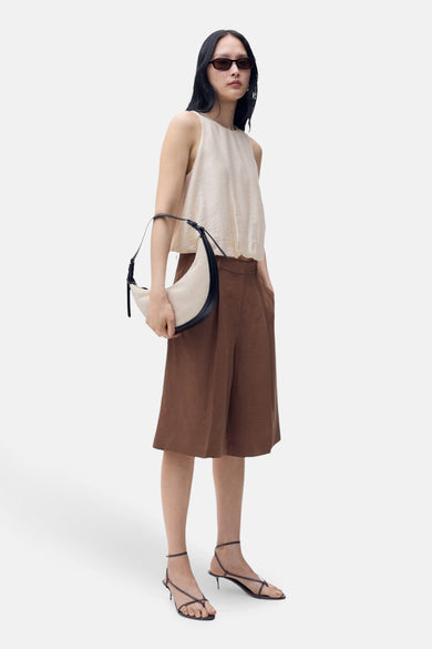 Blouse beige sans manches de MANGO, associée à des culottes marron, un sac épaule blanc et des sandales.