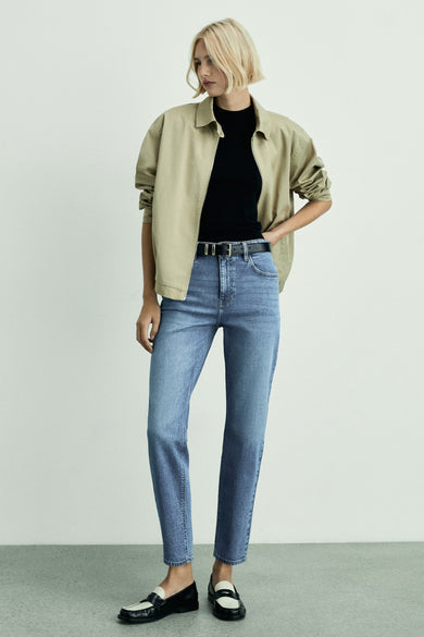 Mid blue mom jeans van MANGO, gedragen met een zwarte top, beige jas en zwart-witte loafers.
