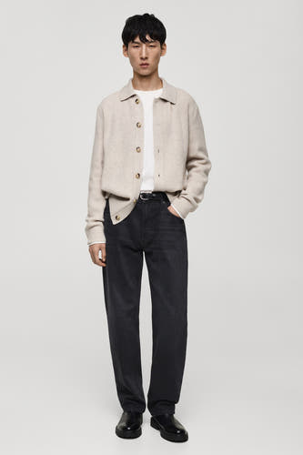 Jean droit en denim gris foncé de MANGO, associé à une veste beige et des chaussures noires en cuir.