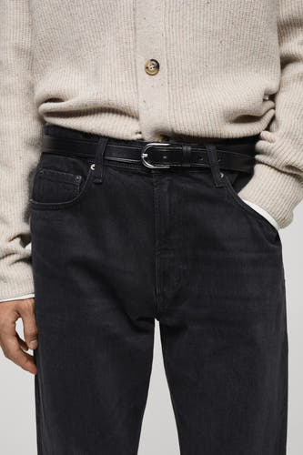 Jean droit en denim gris foncé de MANGO, porté avec un gilet tricoté beige et une ceinture noire.