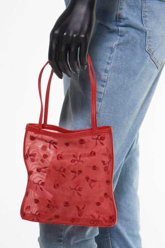 Rode handtas van MANGO, met geborduurde bloemmotieven, vastgehouden door een zwarte mannequinhand en getoond tegen een achtergrond van spijkerstof.
