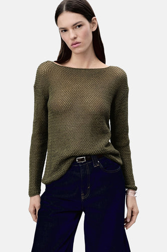 Model in olijfgroene gebreide trui met lange mouwen en donkerblauwe jeans.