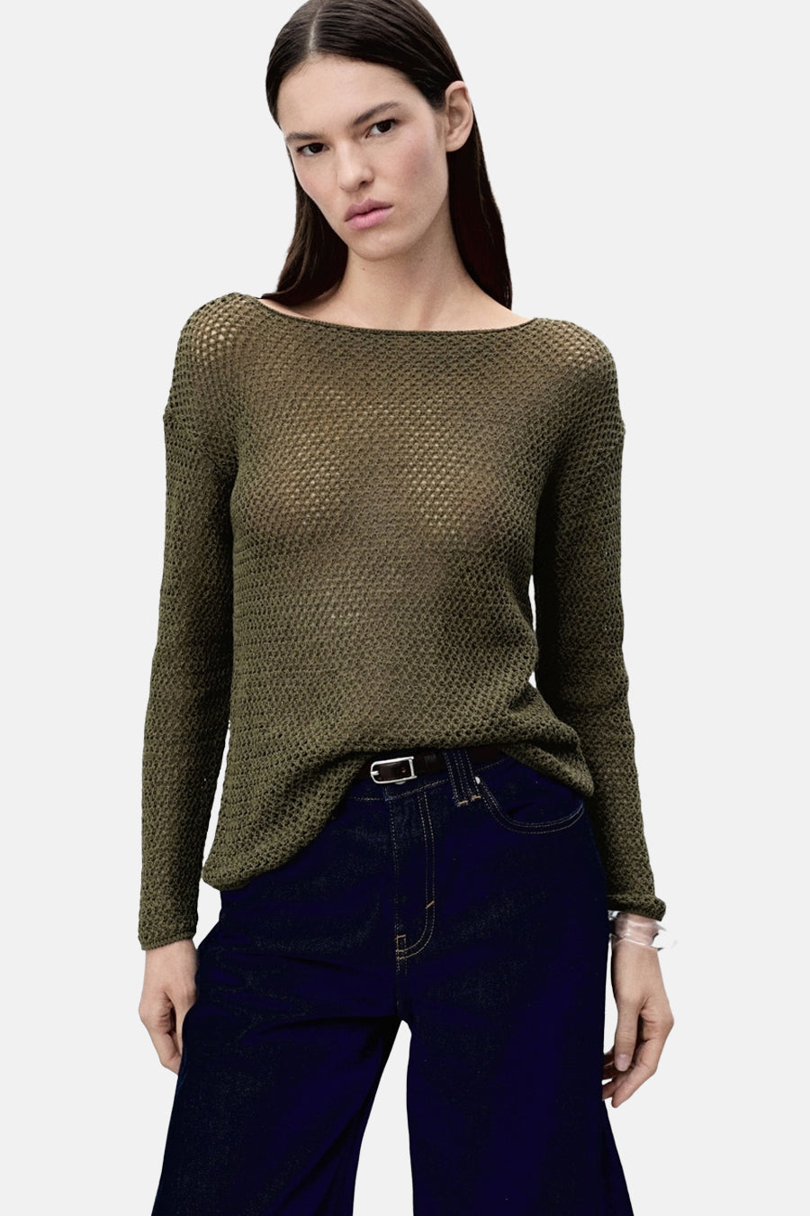 Model in olijfgroene gebreide trui met lange mouwen en donkerblauwe jeans.