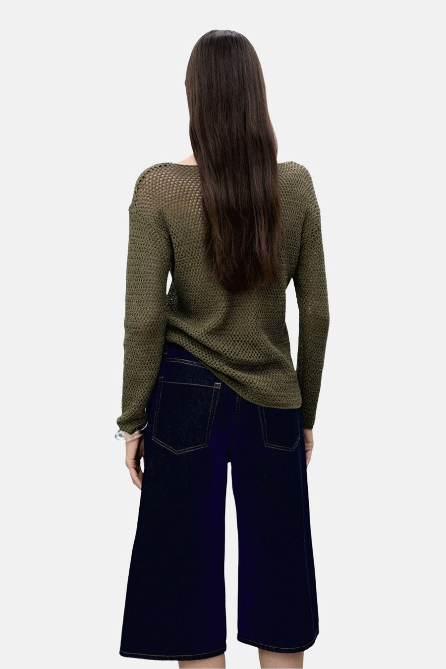 Achterkant van een vrouw in een groene trui en donkere jeans culottes.