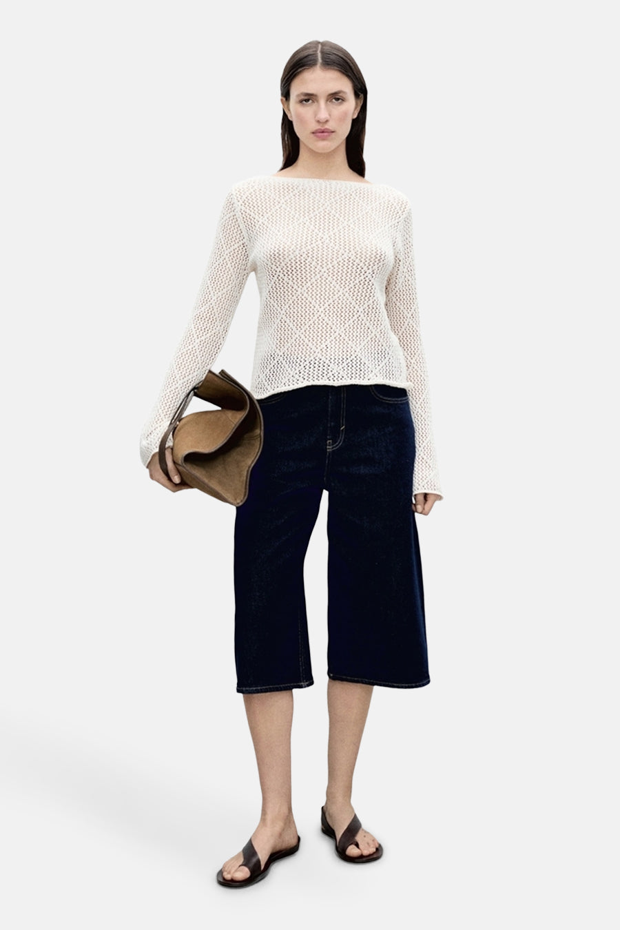 Ecru ronde hals trui van MANGO, met een open gebreide textuur, gecombineerd met donkere denim bermuda en leren sandalen.
