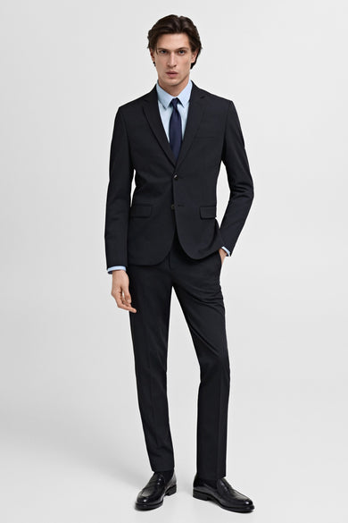 Man in zwart pak en lichtblauw overhemd staand.
