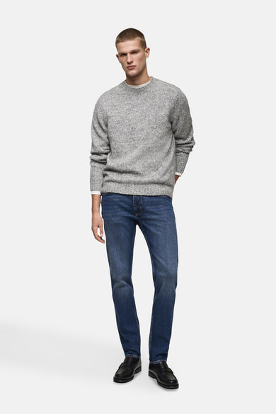 Slim fit jeans van MANGO in mid blue denim, gedragen met een grijze trui en zwarte schoenen.
