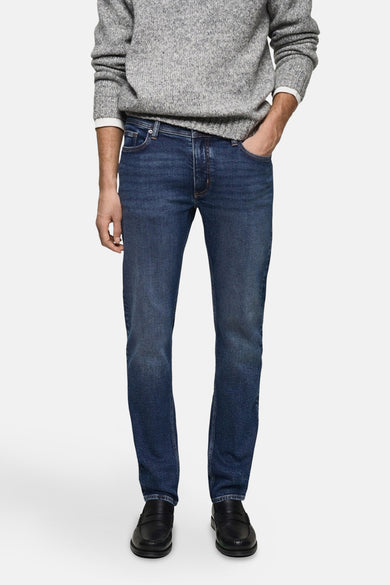 Slim fit jeans van mid blue denim van MANGO, gedragen met een grijze trui en zwarte loafers.